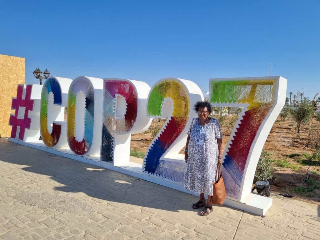 Aunty Rose Elu standing by the Cop27 sign in Egypt - Regenerative Story