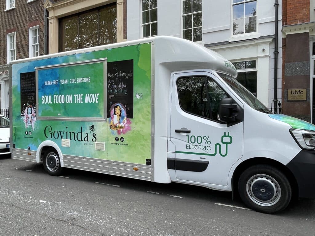 Picture of an electric white van decorated with colourful green and blue patterns with the slogan "Soul Food on the Move".