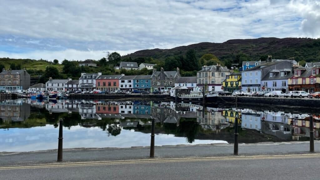 A photo taken by Aden shows the regenerative community of Tarbert - a row of pink, blue and white houses reflected in the water of the harbour, and green hills in the background.